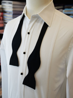 Tuxedo shirt on a mannequin with a black bow tie around the neck, untied.